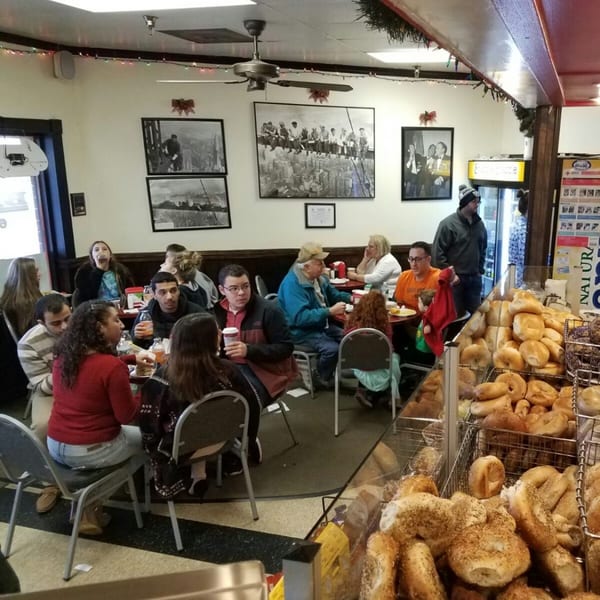 Customers enjoying bagels and coffee inside Bagels N' Cream, with fresh bagels displayed prominently.