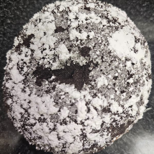A dark, round chocolate bagel is generously dusted with white powdered sugar.