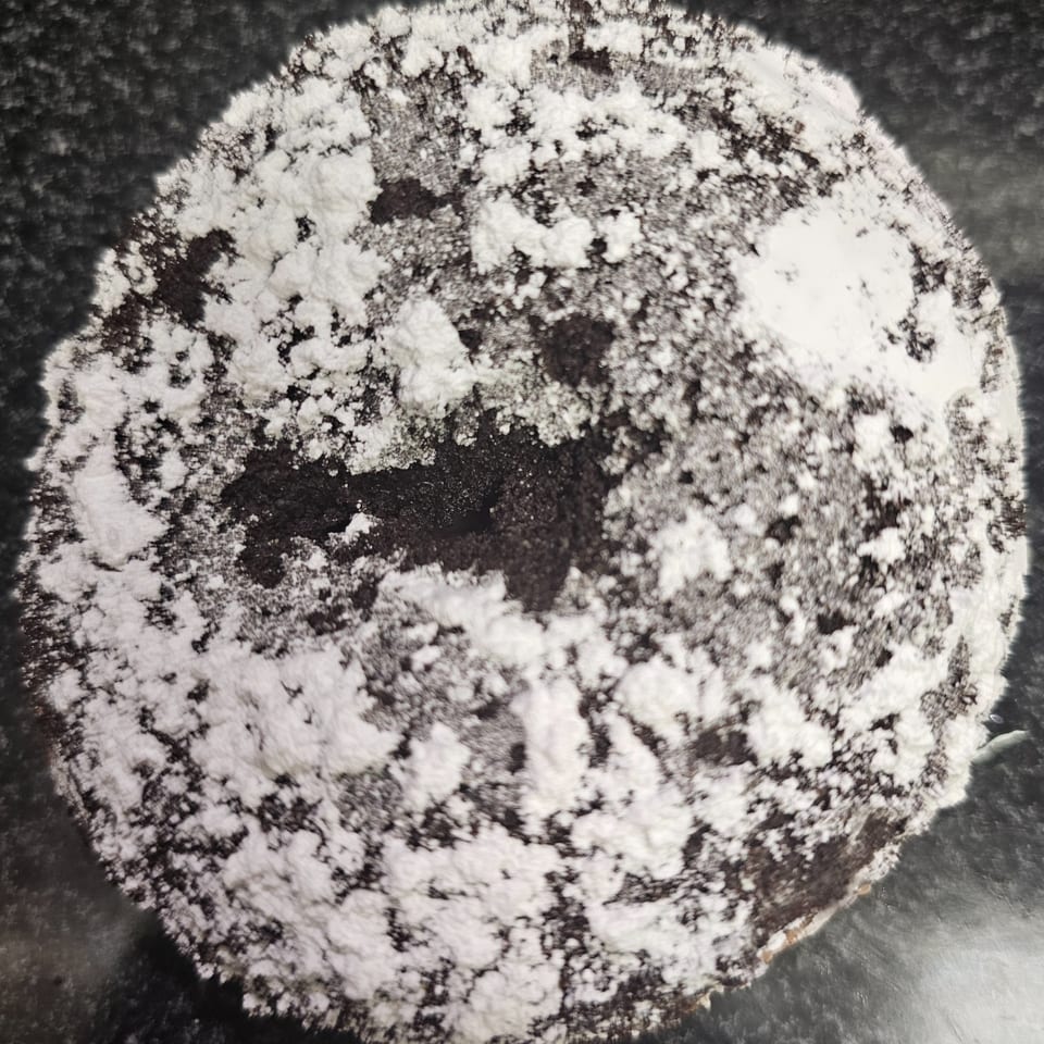 A dark, round chocolate bagel is generously dusted with white powdered sugar.