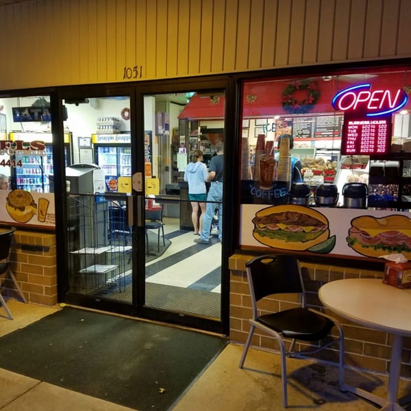 Exterior of Bagels N' Cream at night, with an "OPEN" sign and customers inside.