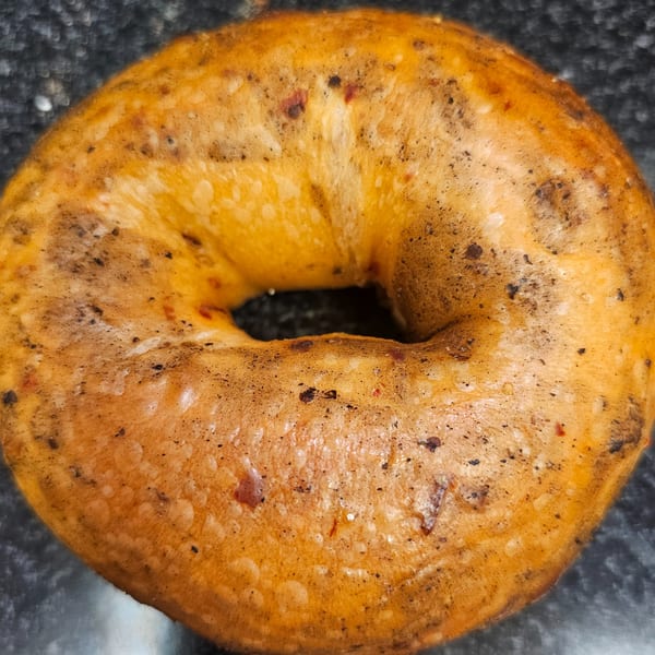 Close-up of a golden-brown bagel from Bagels N' Cream, speckled with dark seasonings.