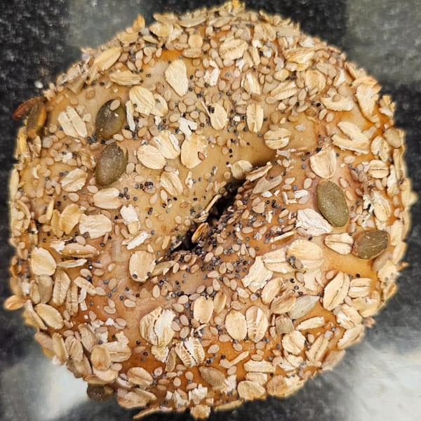 Overhead view of a Bagels N' Cream bagel topped with oats, poppy seeds, and pumpkin seeds.