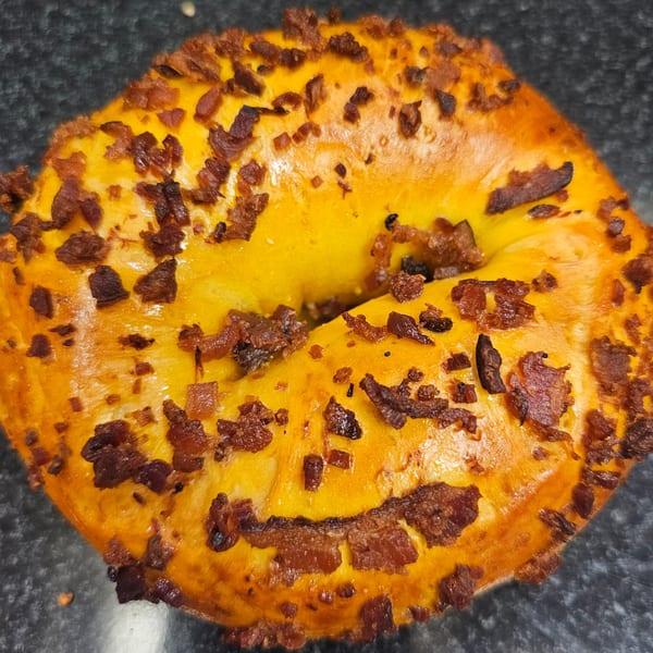 Close-up of a golden bagel from Bagels N' Cream, generously topped with crispy bacon bits.