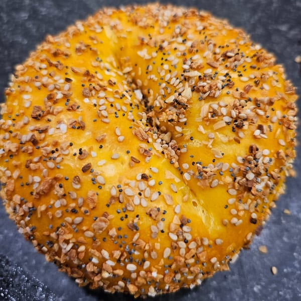 Close-up of a golden-brown everything bagel from Bagels N' Cream, topped with seeds and garlic.