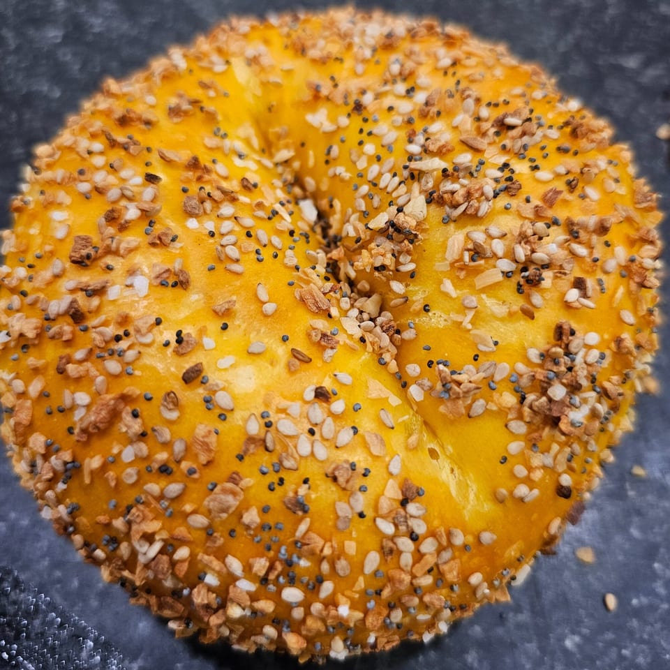Close-up of a golden-brown everything bagel from Bagels N' Cream, topped with seeds and garlic.