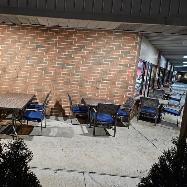 Outdoor patio seating at Bagels N' Cream with several tables and blue-cushioned chairs against a brick wall.