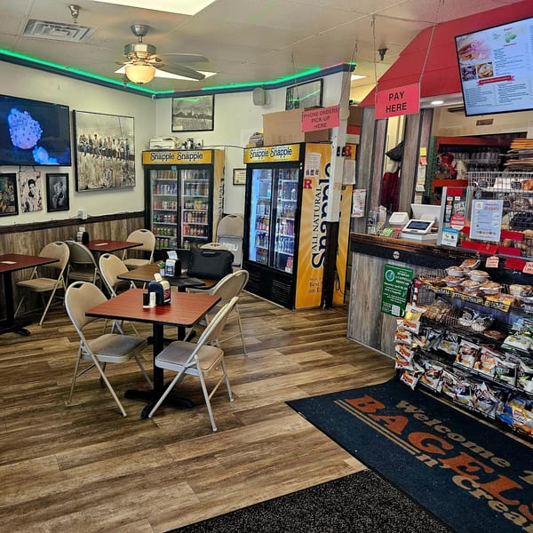 Interior of Bagels N' Cream showing tables, Snapple refrigerators, and a counter with bagels and snacks.