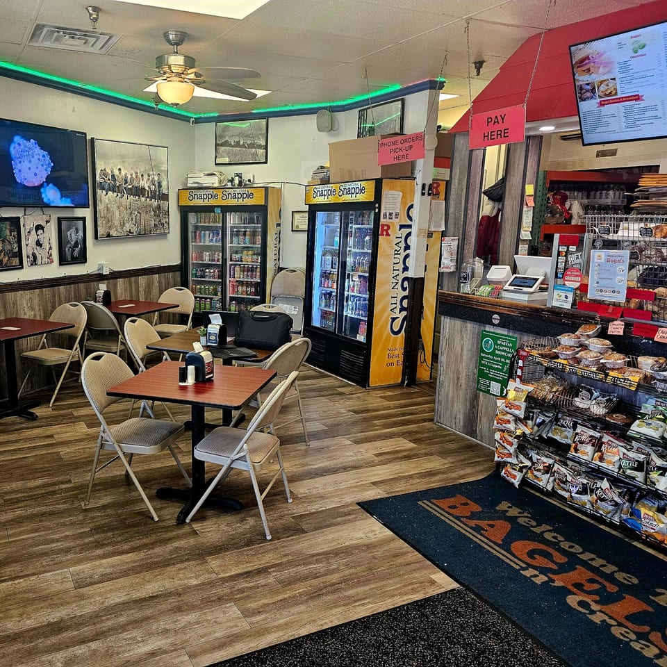 Interior of Bagels N' Cream showing tables, Snapple refrigerators, and a counter with bagels and snacks.