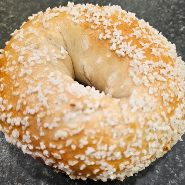 A close-up of a golden-brown bagel from Bagels N' Cream, generously topped with coarse salt.