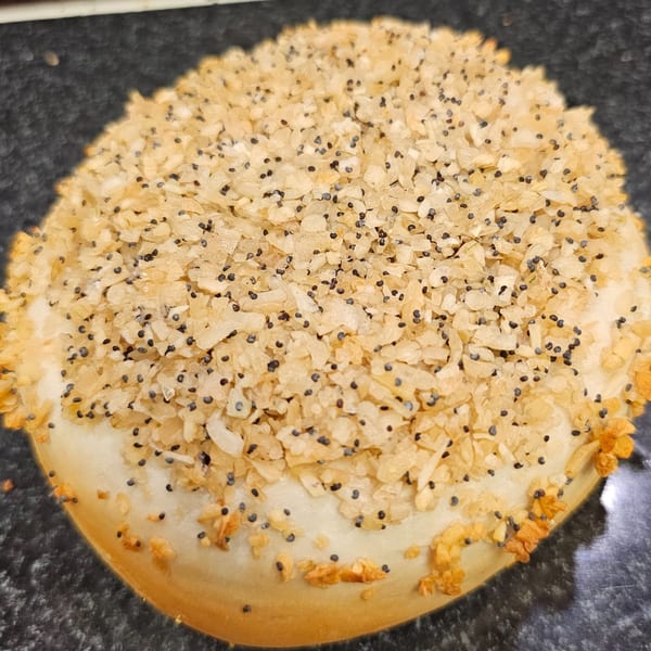 Close-up of a Bagels N' Cream everything bagel, generously topped with poppy seeds and dried garlic.
