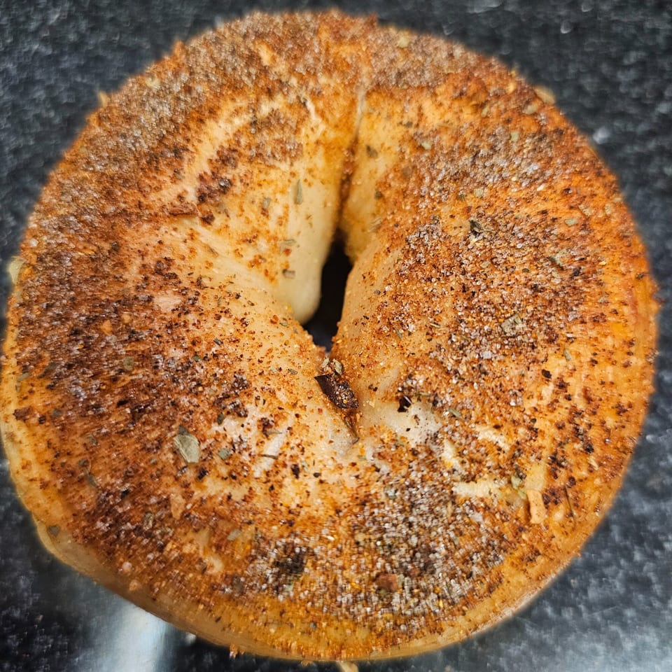 A close-up of a Bagels N' Cream bagel, generously topped with everything seasoning.