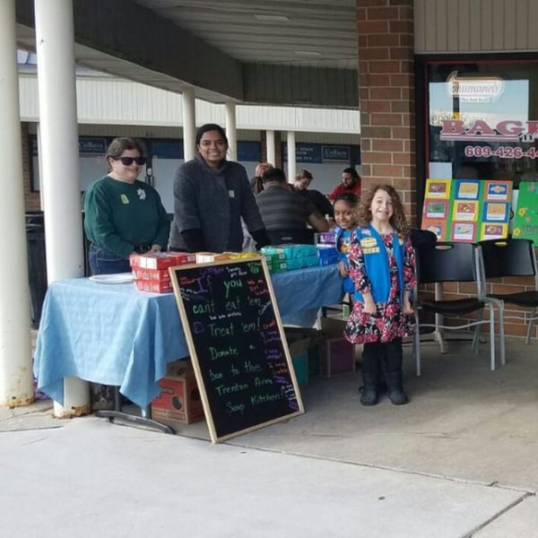 People, including a Girl Scout, selling cookies at a table outside Bagels N' Cream.