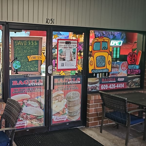 The storefront of Bagels N' Cream, featuring promotional signs for bagels, sandwiches, and coffee.