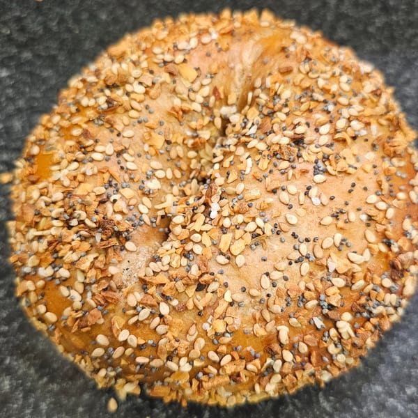 Close-up of a Bagels N' Cream everything bagel, generously topped with seeds and garlic.