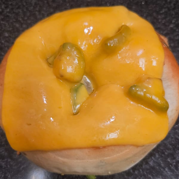 A bagel topped with melted yellow cheese and green chili pieces on a dark surface.