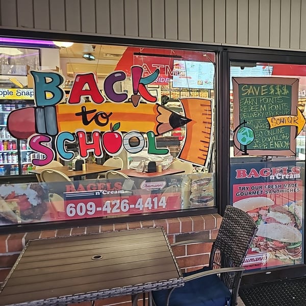 Bagels N' Cream storefront window with a colorful "Back to School" sign and promotional posters.