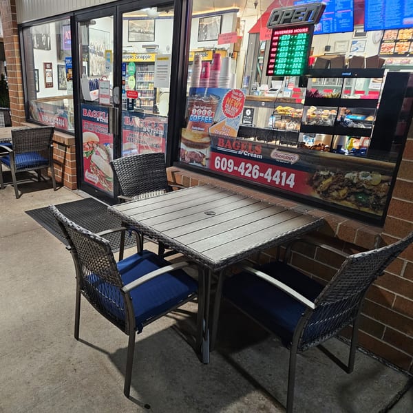 Outdoor seating with two tables and chairs in front of Bagels N' Cream, showcasing bagels and coffee.