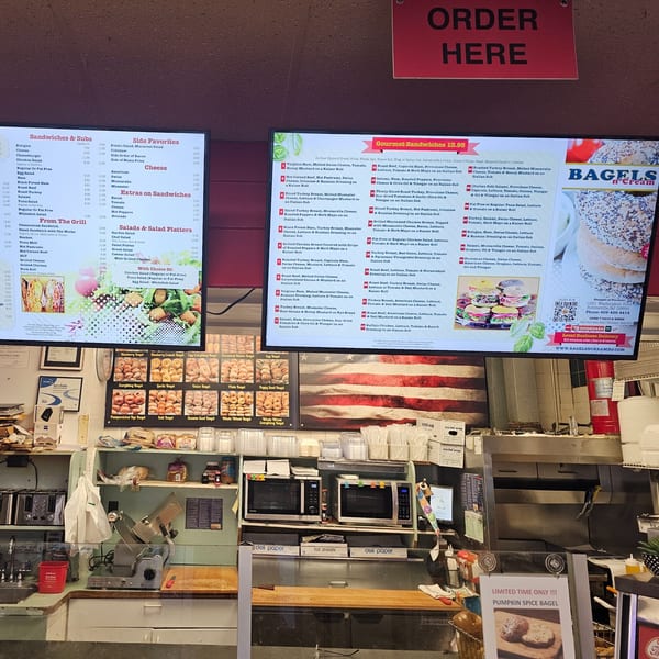 A Bagels N' Cream deli counter with menu boards, bagel displays, and kitchen equipment.