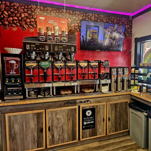 A self-serve coffee station at Bagels N' Cream with various coffee dispensers and a cappuccino machine.