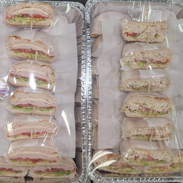 Two catering trays filled with individually wrapped Bagels N' Cream sandwiches, some turkey and some chicken salad.