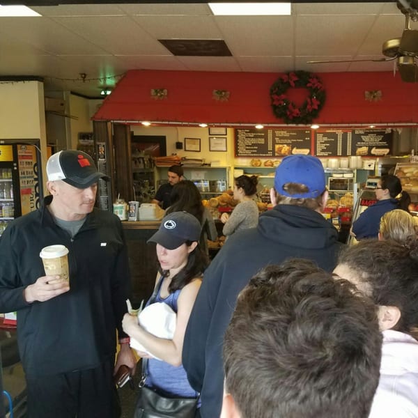 Customers line up inside Bagels N' Cream, with menu boards and bagels visible behind the counter.