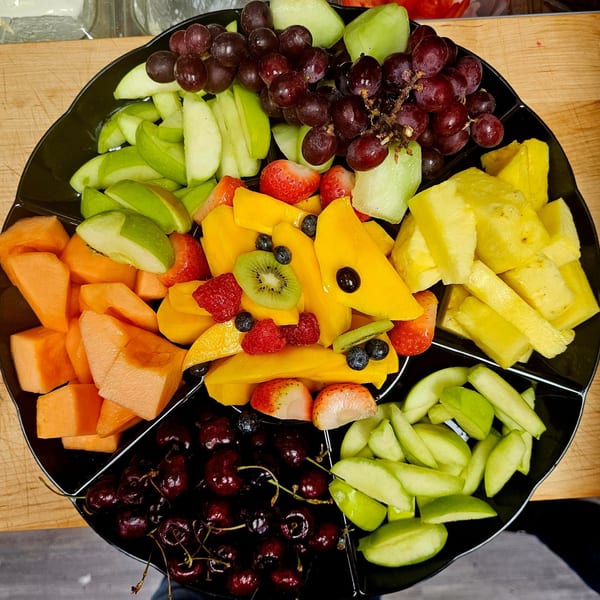 A black platter filled with various fresh fruits, including grapes, melon, pineapple, and berries.