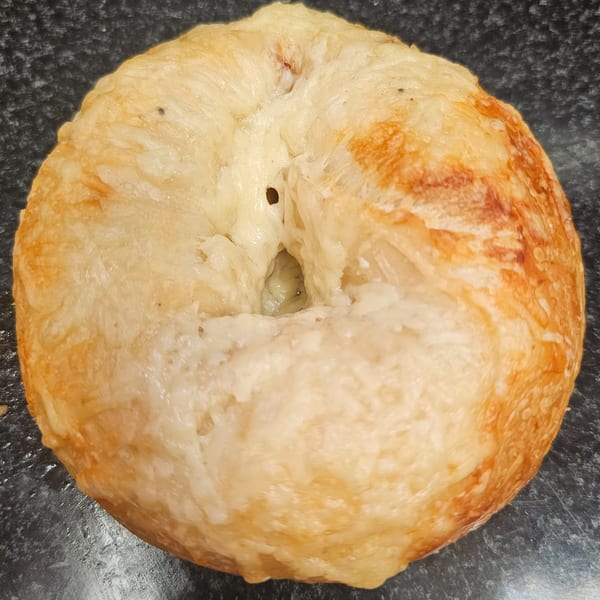 A golden-brown cheese bagel from Bagels N' Cream, close-up on a dark surface.