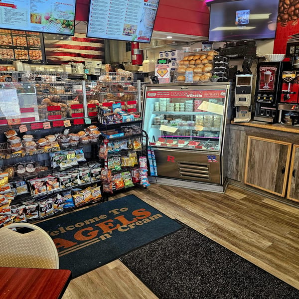 Interior view of Bagels N' Cream, showing shelves of bagels, muffins, chips, and a refrigerated display.